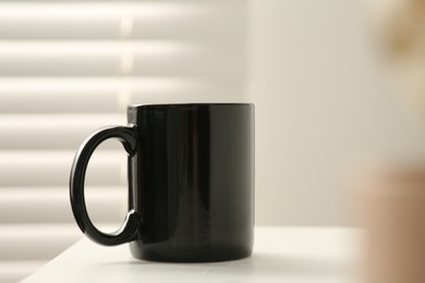 Photo of Black mug on white table indoors. Mockup for design