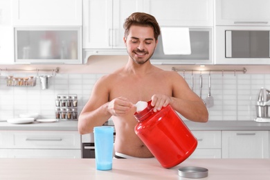 Photo of Young shirtless man preparing protein shake at table in kitchen