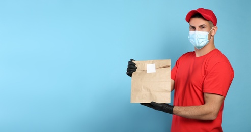 Courier in medical mask holding paper bag with takeaway food on light blue background, space for text. Delivery service during quarantine due to Covid-19 outbreak