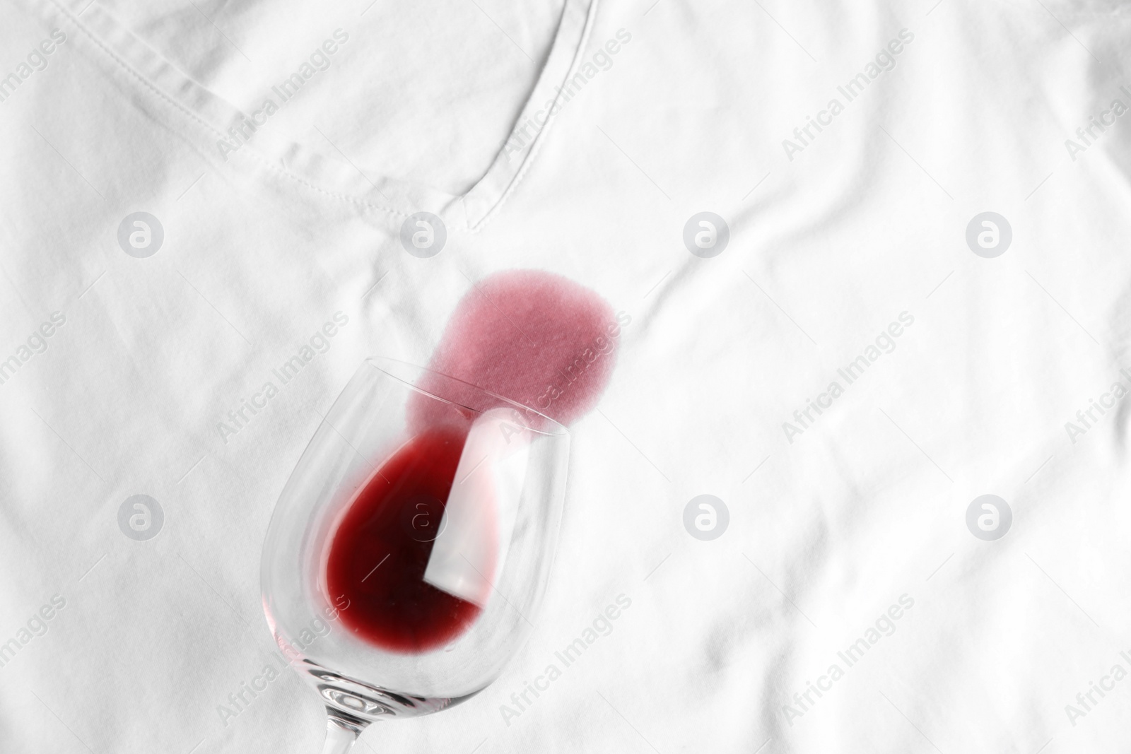 Photo of Overturned glass and spilled exquisite red wine on white t-shirt, top view. Space for text