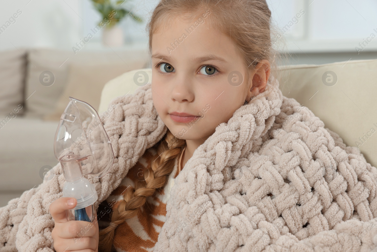 Photo of Little girl holding nebulizer for inhalation at home