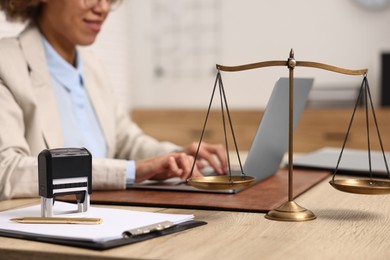 Notary using laptop at workplace in office, focus on scales of justice