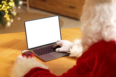 Photo of Merry Christmas. Santa Claus with cup of drink using laptop, closeup