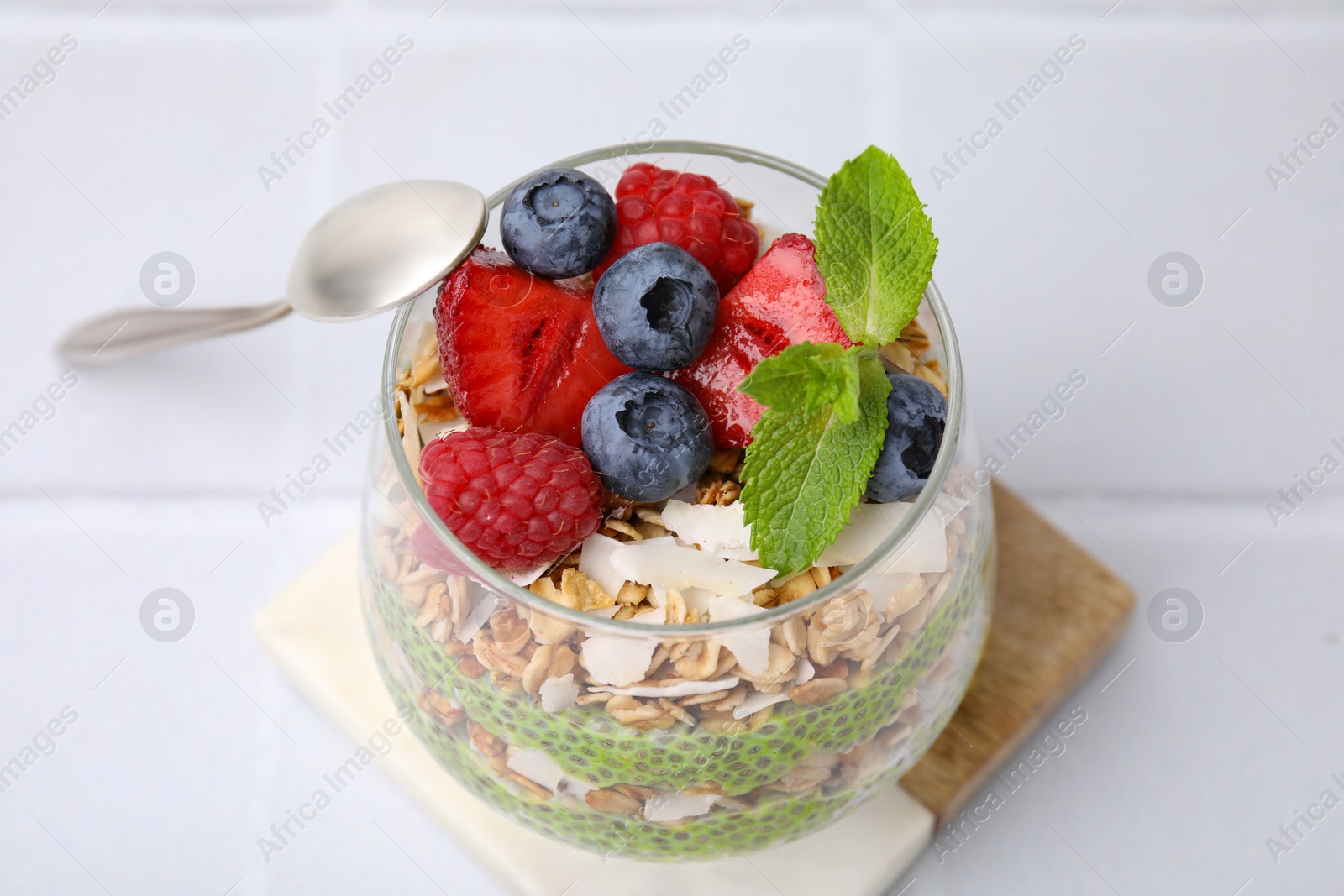 Photo of Tasty oatmeal with chia matcha pudding and berries on white tiled table, above view. Healthy breakfast