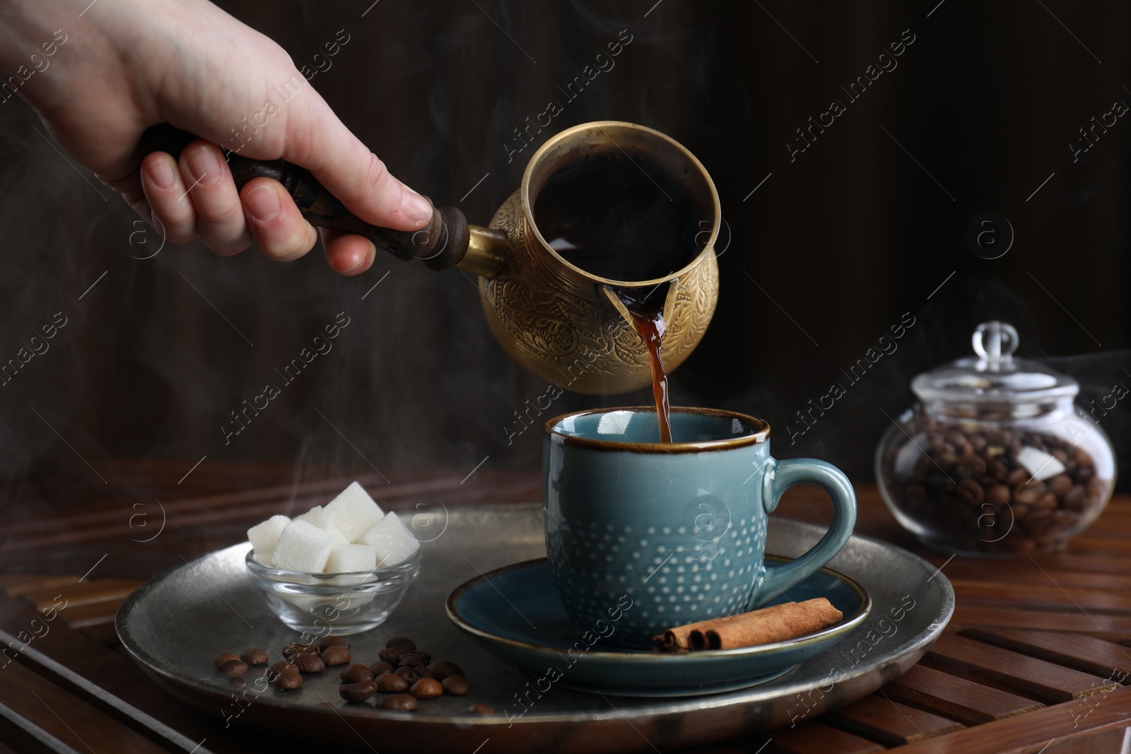 Photo of Turkish coffee. Woman pouring brewed beverage from cezve into cup at wooden table, closeup