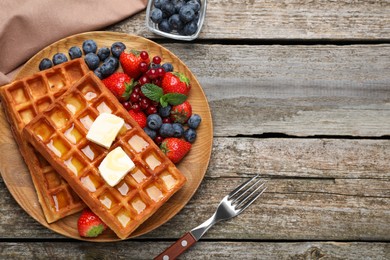 Plate of delicious Belgian waffles with honey, berries and butter on wooden table, flat lay. Space for text
