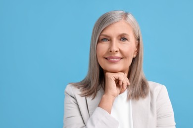 Portrait of beautiful middle aged woman on light blue background, space for text
