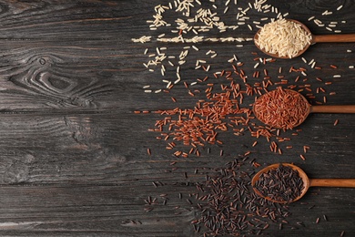 Photo of Brown rice varieties in wooden spoons on table, flat lay. Space for text