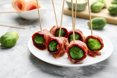 Plate with Brussels sprouts wrapped in bacon on grey table, closeup