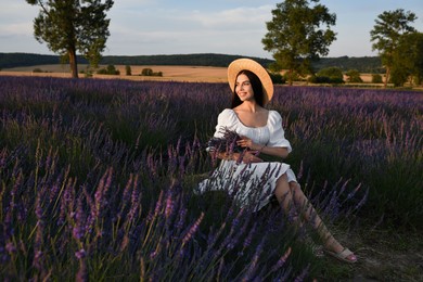 Beautiful young woman sitting in lavender field at sunset