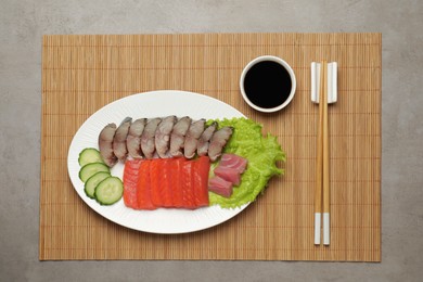 Photo of Delicious mackerel, salmon and tuna served with cucumbers, lettuce and soy sauce on grey table, top view. Tasty sashimi dish