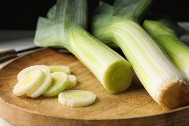 Photo of Fresh raw leeks on wooden tray, closeup. Ripe onion