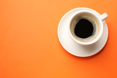 Fresh coffee in cup on orange background, top view. Space for text