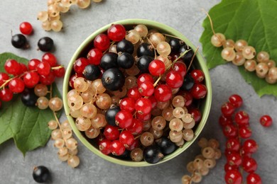 Photo of Different fresh ripe currants and green leaves on light grey table, flat lay