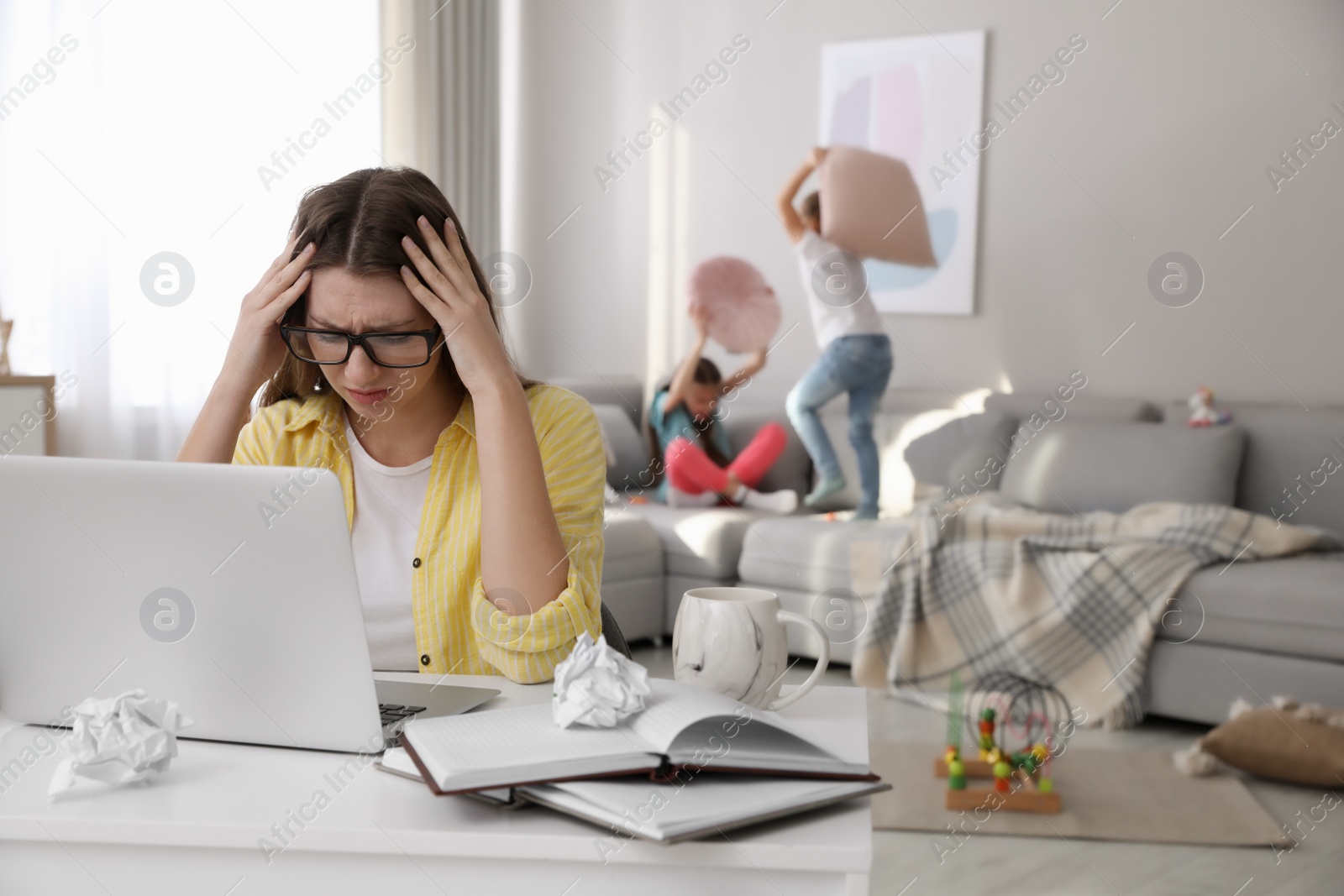 Photo of Children disturbing stressed woman in living room. Working from home during quarantine