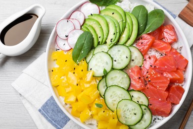 Delicious poke bowl with salmon and vegetables served on wooden table, flat lay