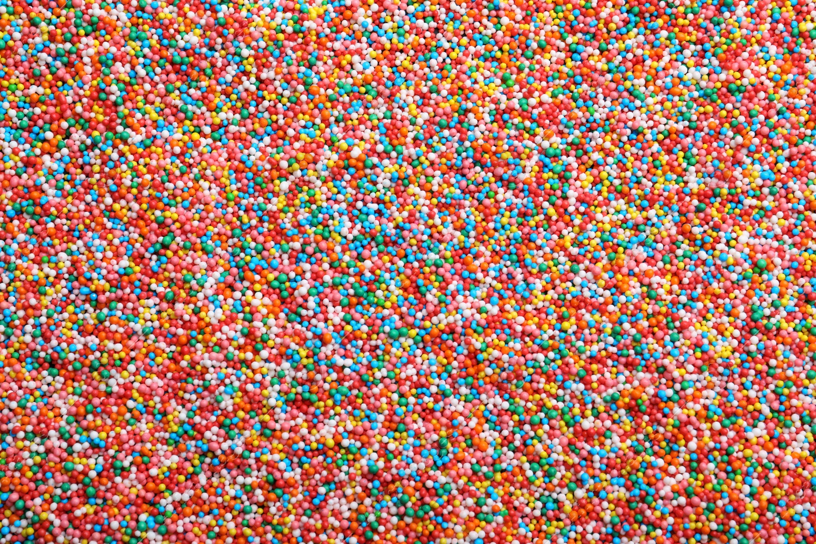 Photo of Bright colorful sprinkles as background, top view. Confectionery decor