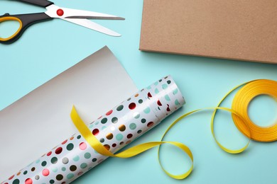 Photo of Wrapping paper roll, ribbon, scissors and box on turquoise background, flat lay
