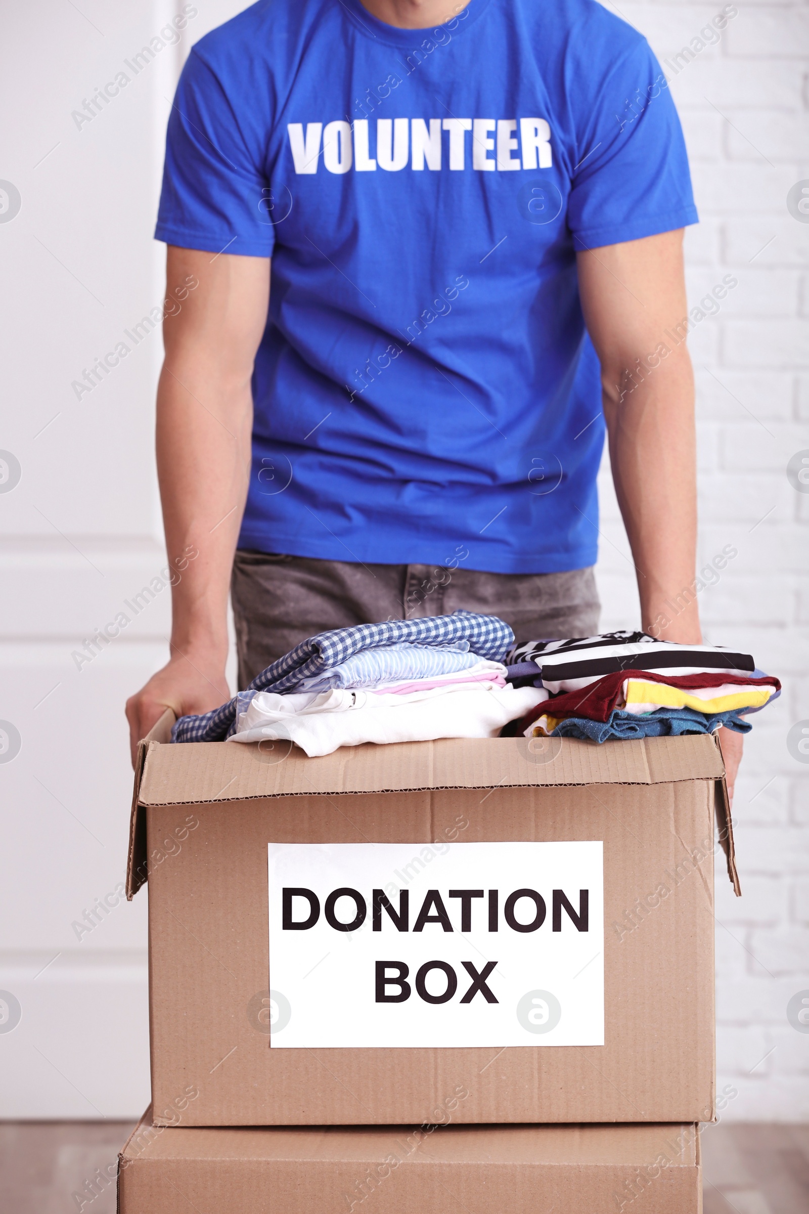 Photo of Male volunteer holding donation box with clothes indoors