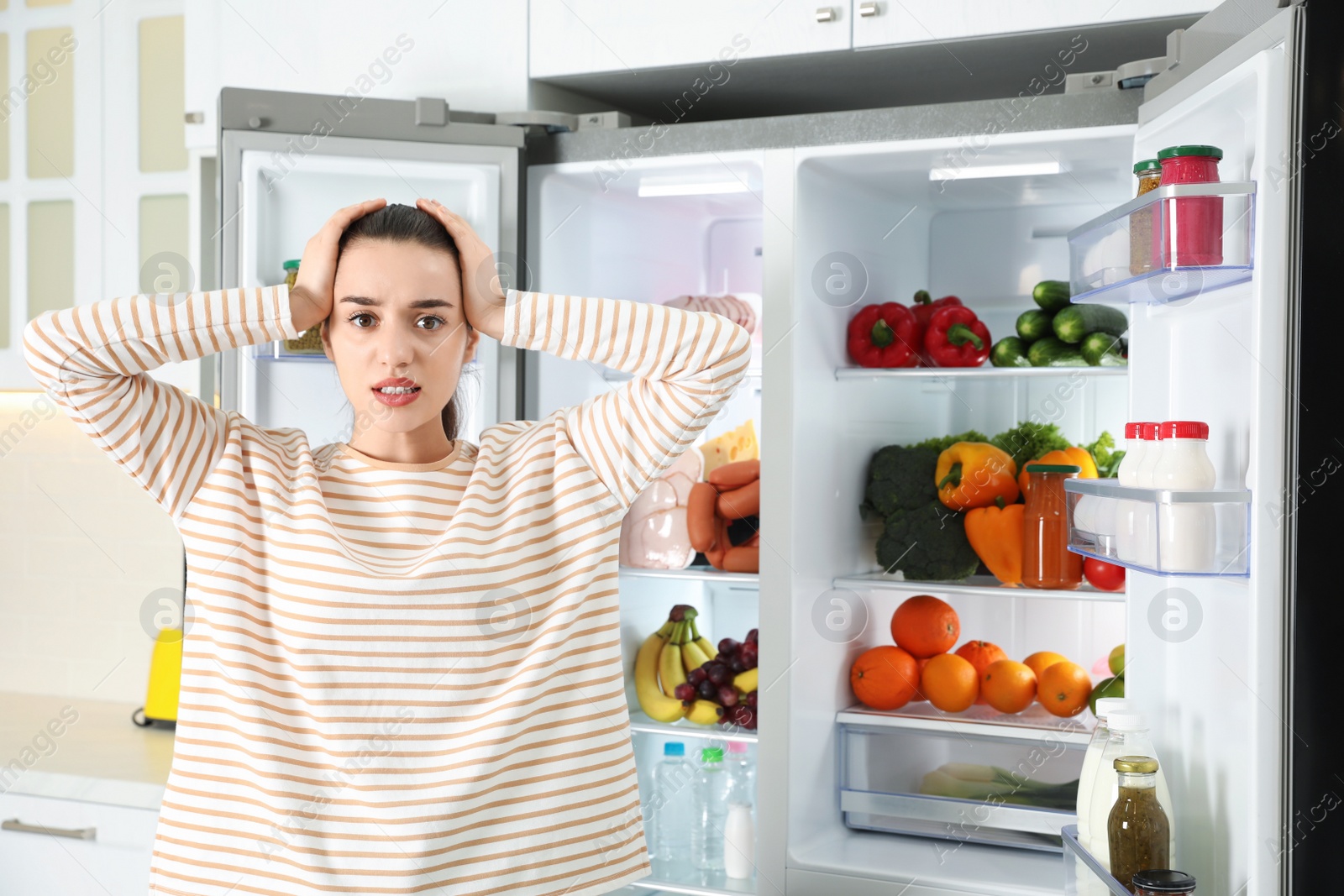 Photo of Emotional young woman near open refrigerator in kitchen