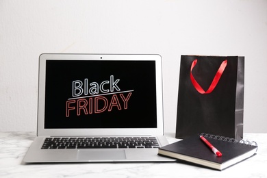Laptop, shopping bag, notebook and pen on white marble table. Black Friday Sale online