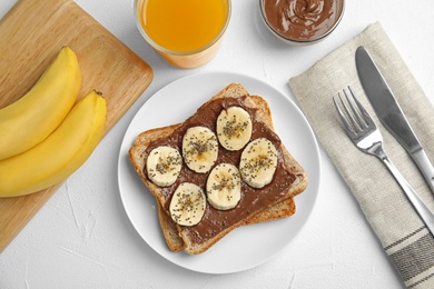 Photo of Slice of bread with chocolate paste and banana on white table, flat lay