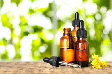 Bottles of essential oil and flowers on wooden table against blurred background. Space for text