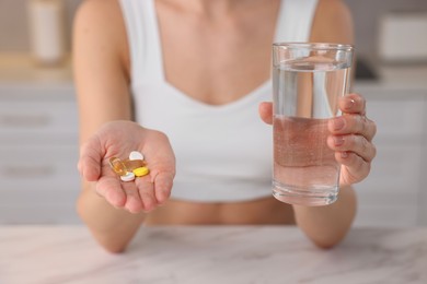 Woman with glass of water and pills at table indoors, closeup. Weight loss