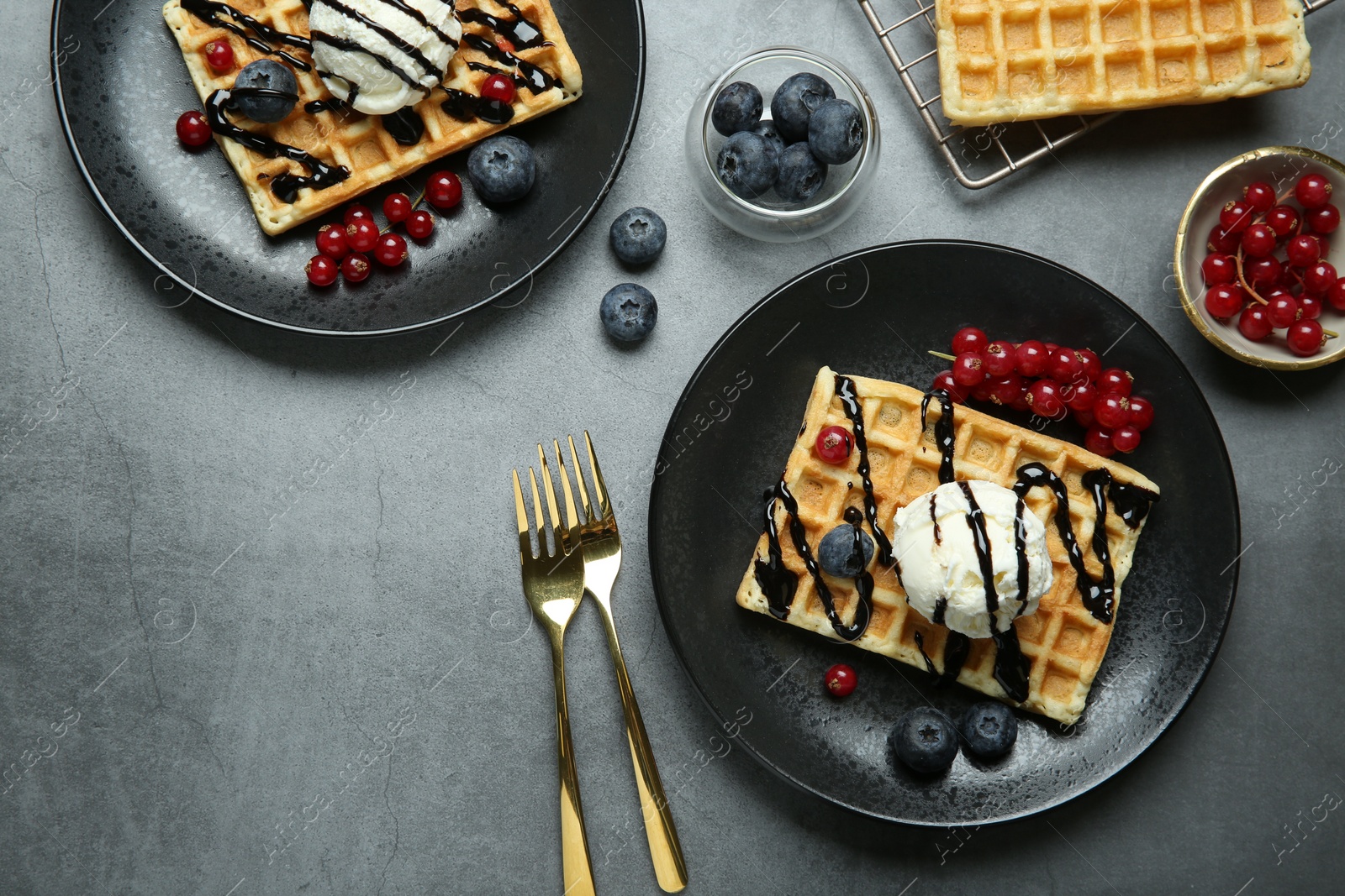 Photo of Delicious Belgian waffles with ice cream, berries and chocolate sauce on grey textured table, flat lay. Space for text