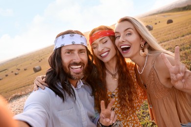 Photo of Happy hippie friends showing peace signs while taking selfie in field