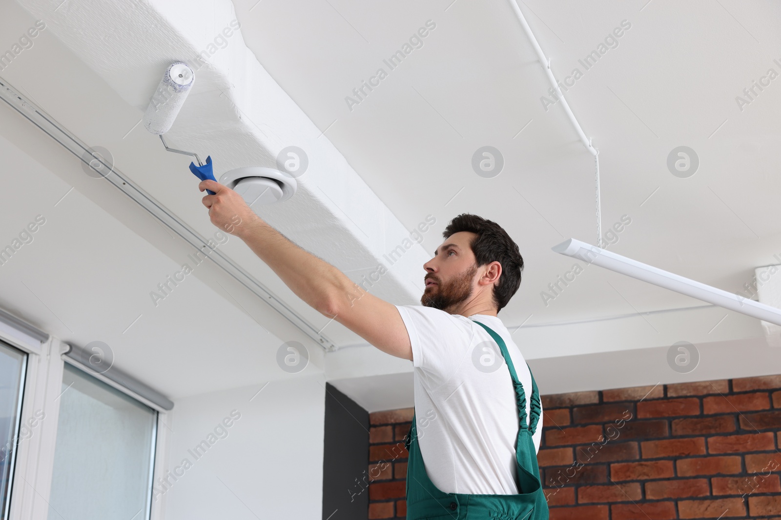 Photo of Handyman painting ceiling with roller in room