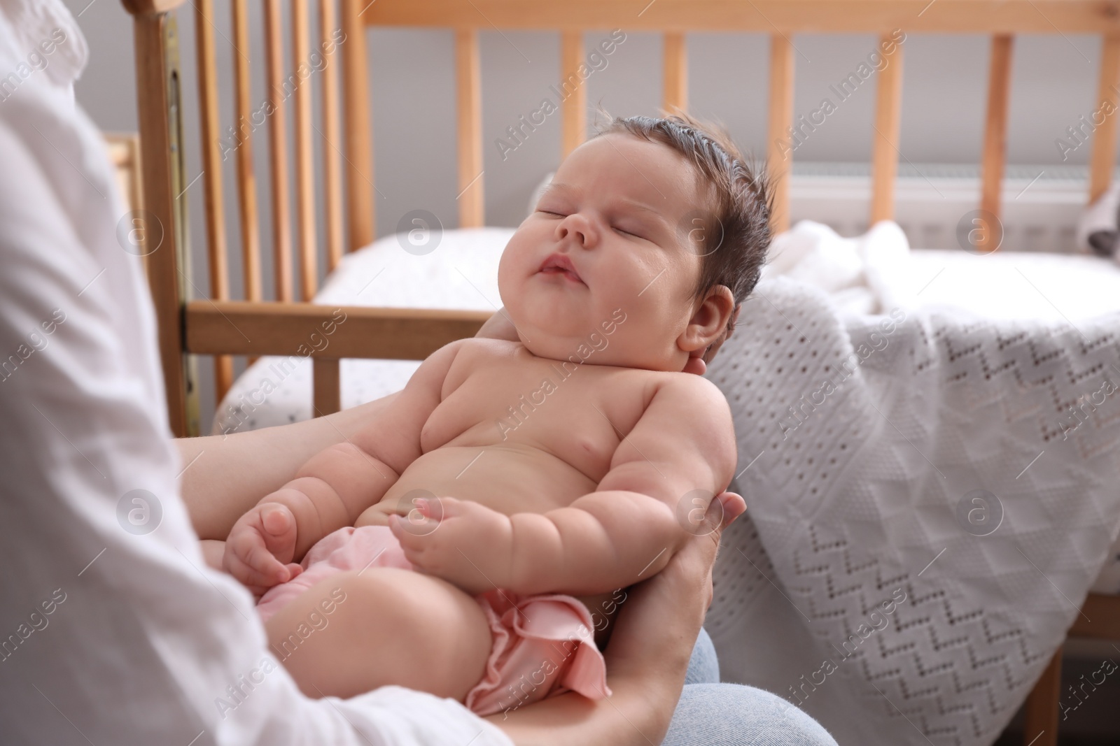 Photo of Mother holding cute sleeping baby near crib at home