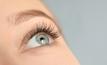 Photo of Young woman with beautiful long eyelashes on gray background, closeup. Extension procedure
