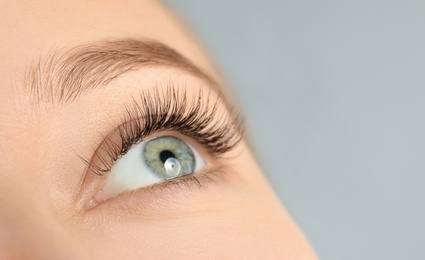 Young woman with beautiful long eyelashes on gray background, closeup. Extension procedure