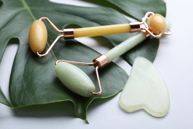 Photo of Gua sha stone, different face rollers and monstera leaf on light background