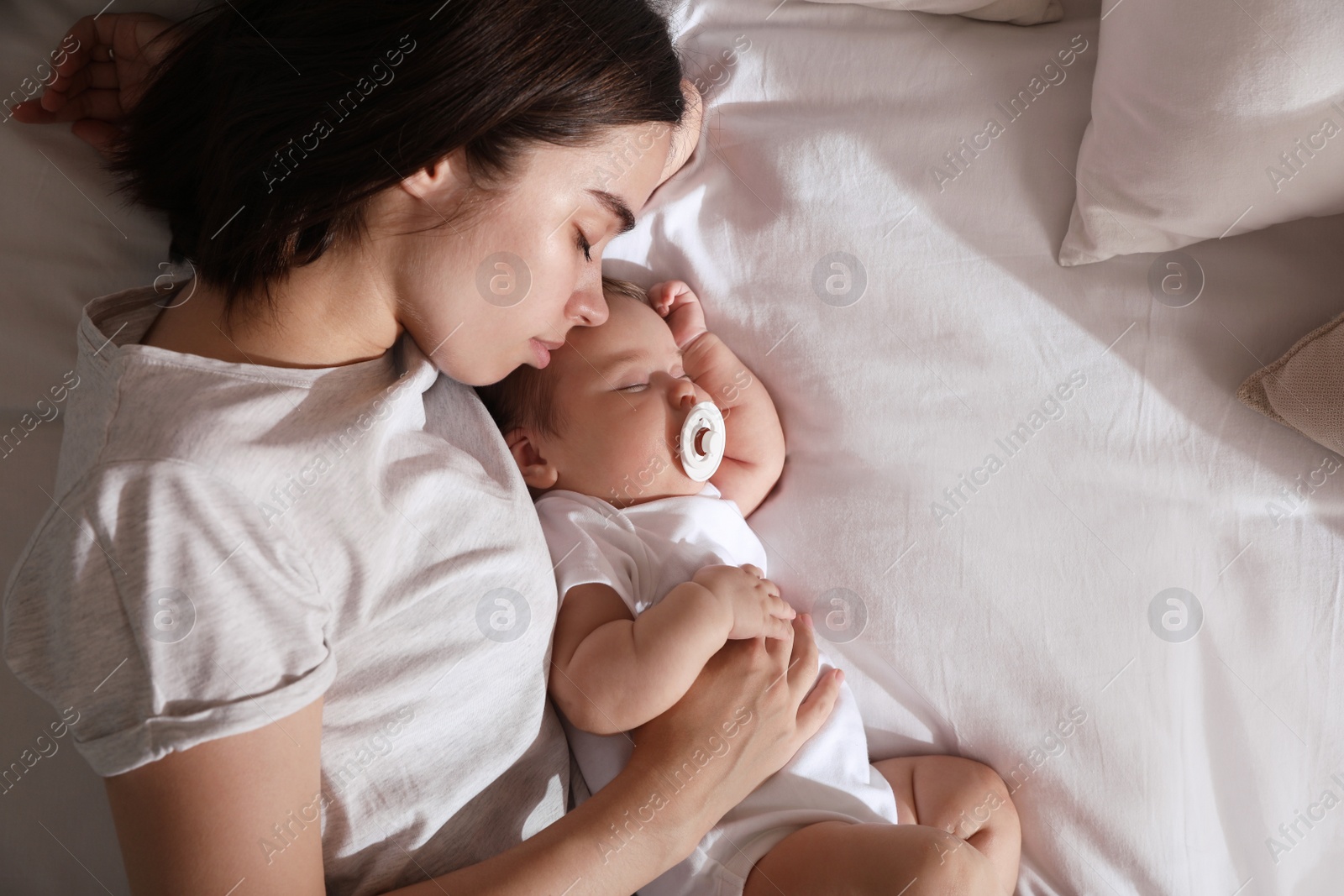 Photo of Young mother resting near her sleeping baby on bed, top view. Space for text