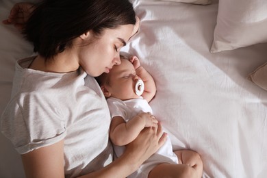 Young mother resting near her sleeping baby on bed, top view. Space for text