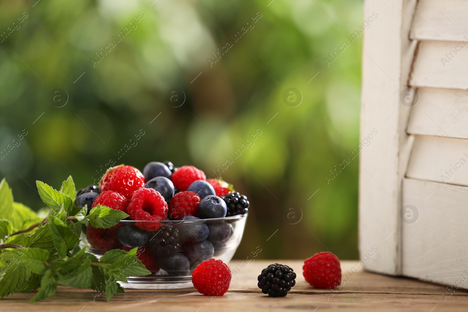 Photo of Glass bowl with different fresh ripe berries and mint on wooden table outdoors