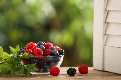 Photo of Glass bowl with different fresh ripe berries and mint on wooden table outdoors