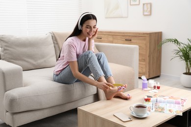 Photo of Beautiful young woman listening to music while giving herself pedicure in living room