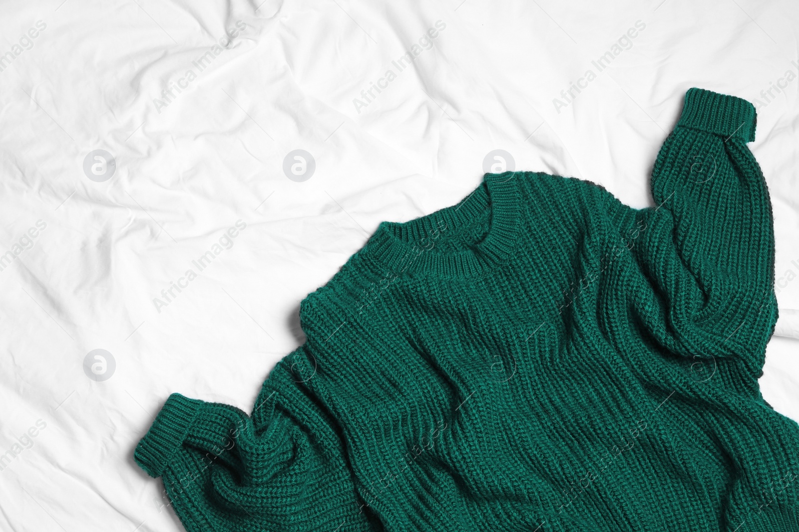 Photo of Dark green knitted sweater on white fabric, flat lay. Space for text