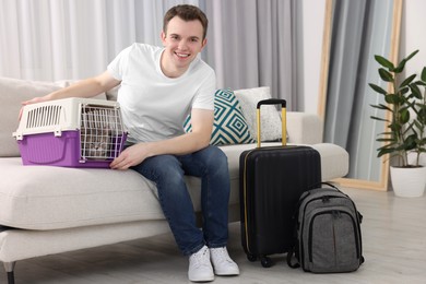 Photo of Travel with pet. Man near carrier with cat on sofa at home