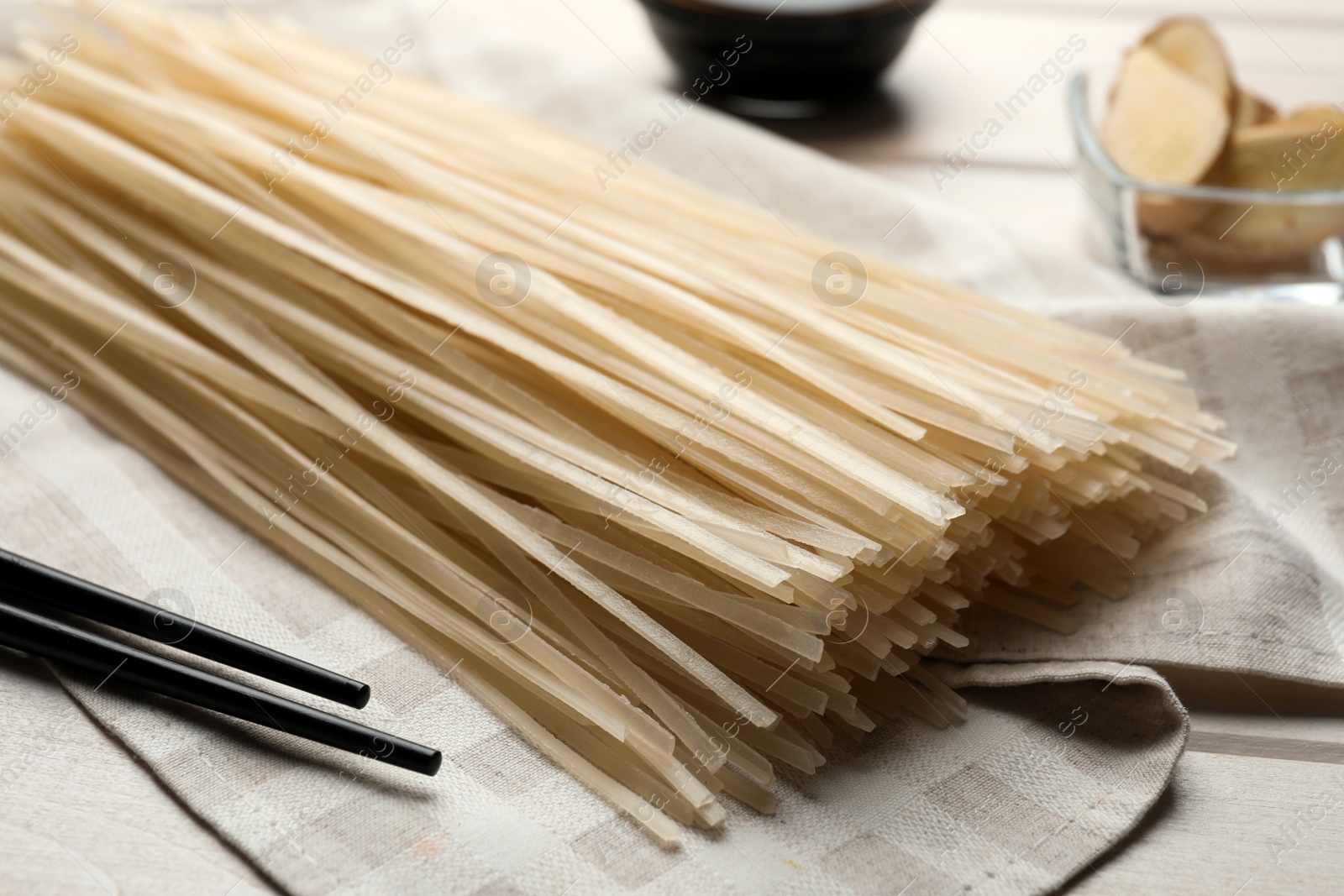 Photo of Uncooked rice noodles and chopsticks on table, closeup