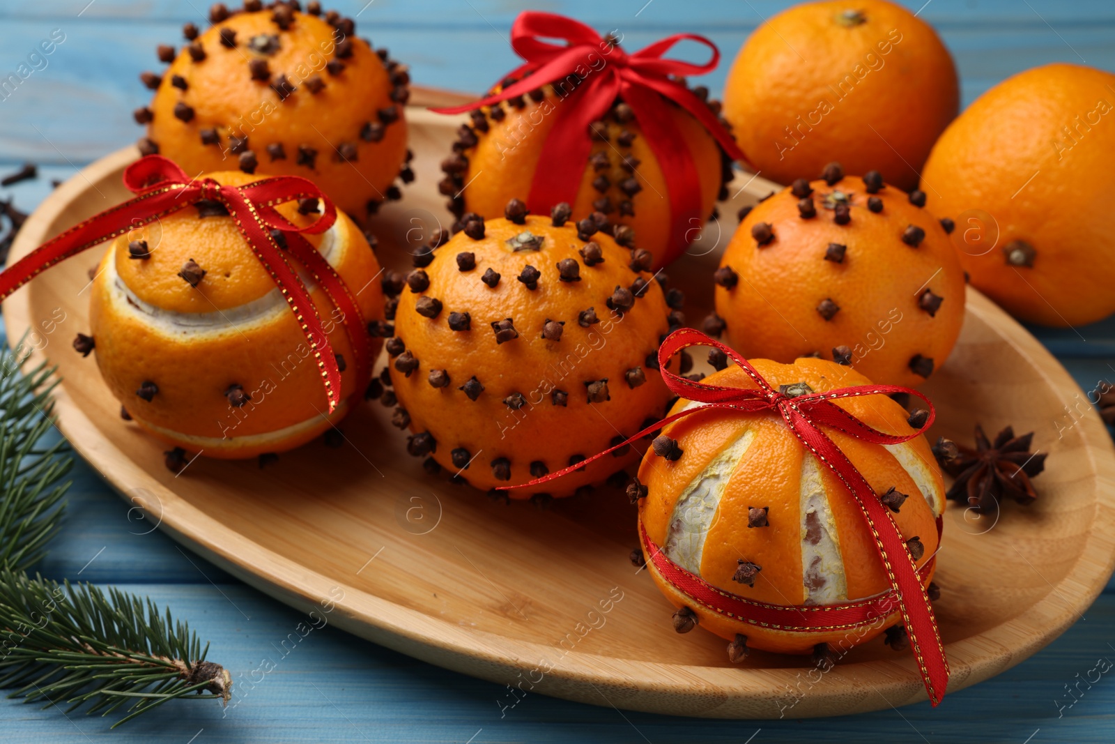 Photo of Pomander balls made of tangerines with cloves and fir branch on light blue wooden table