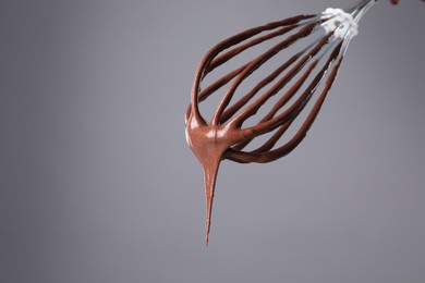 Chocolate cream flowing from whisk on grey background, closeup. Space for text