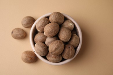 Photo of Whole nutmegs in bowl on light brown background, top view