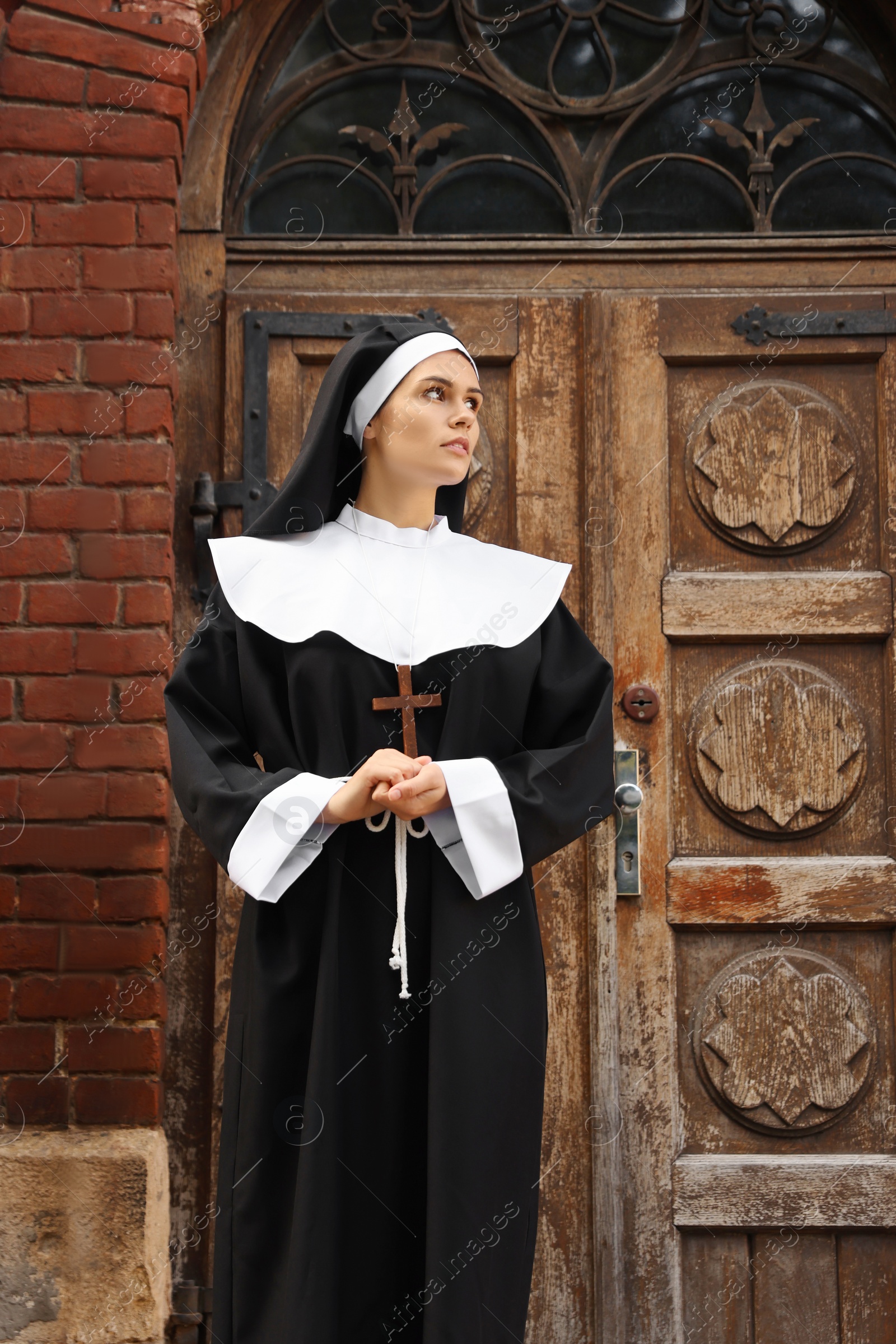 Photo of Young nun with Christian cross near old building outdoors