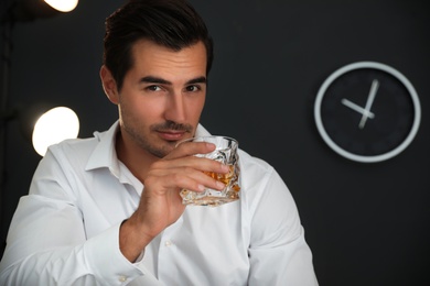 Photo of Young man with glass of whiskey at home. Space for text