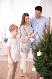 Happy family with cute child decorating Christmas tree together at home