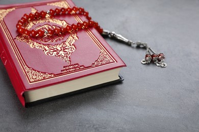 Photo of Muslim prayer beads and Quran on grey stone table, closeup